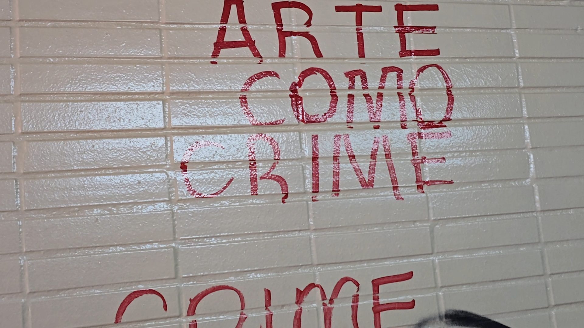 Inscrição “Arte como crime” em spray vermelho sobre azulejo